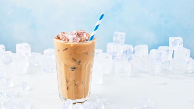 A glass is filled with iced coffee and a blue and white straw.